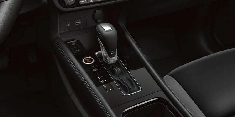 Close-up of a car's black interior, showing the automatic gear shift, engine start/stop button, and console.