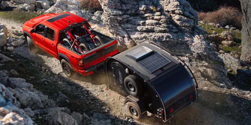 Overhead view of a red pickup truck carrying bikes and towing a black teardrop camper with solar panels, off-roading.