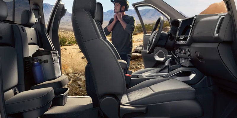 Interior view of a pickup truck with black seats and a person outside putting on a bicycle helmet.