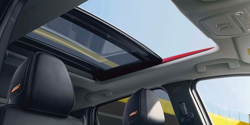 Interior view of a car with a large, open sunroof revealing a bright blue sky.