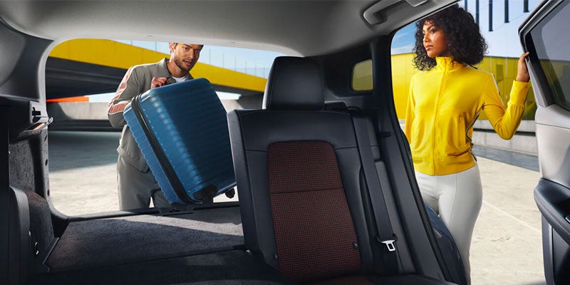 Man loading blue suitcase into car trunk next to woman.