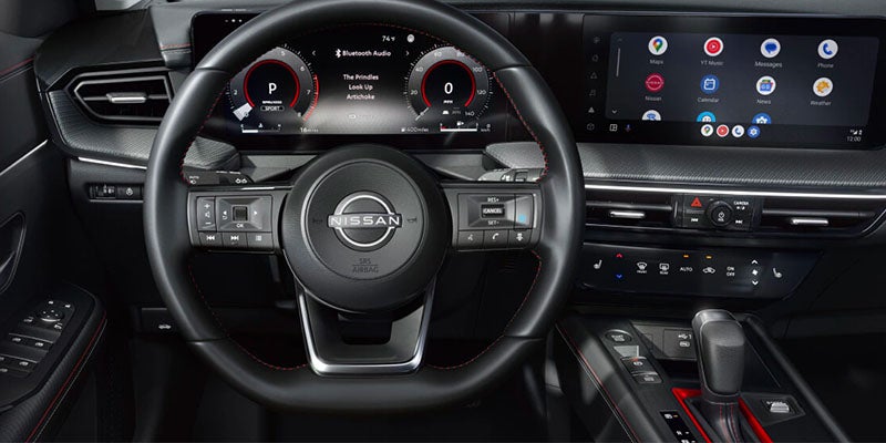 Interior view of a modern car dashboard with a Nissan steering wheel, digital instrument cluster, and touchscreen infotainment system.