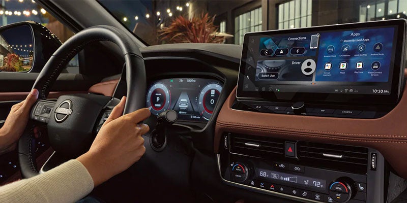 Hands on a car steering wheel; the dashboard features a digital display and an infotainment screen with various apps.