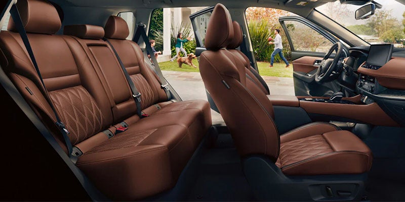 Interior view of a car with brown leather seats, a family and dog playing outside.