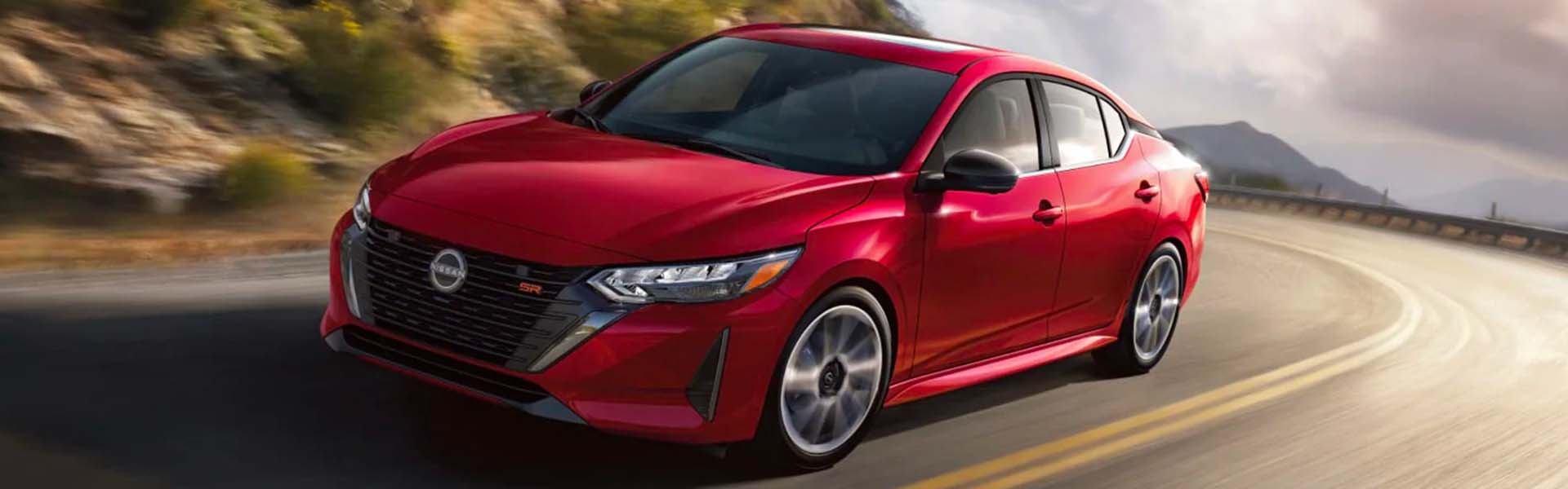A red Nissan Sentra SR moving quickly on a winding mountain road with blurred background elements.