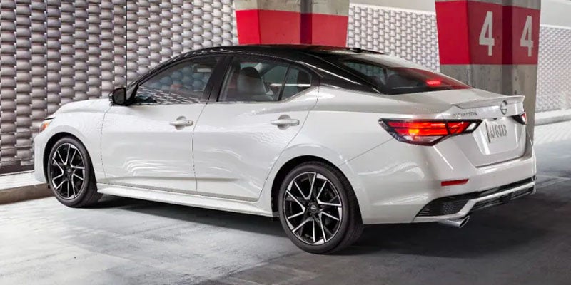 Rear three-quarter view of a white Nissan Sentra with a black roof, parked in an urban garage.